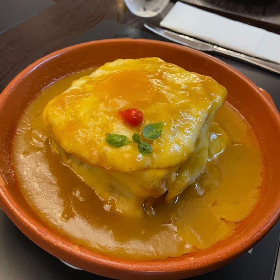 Francesinha do Restaurante O Vareiro em prato de barro, coberta de queijo derretido e molho
